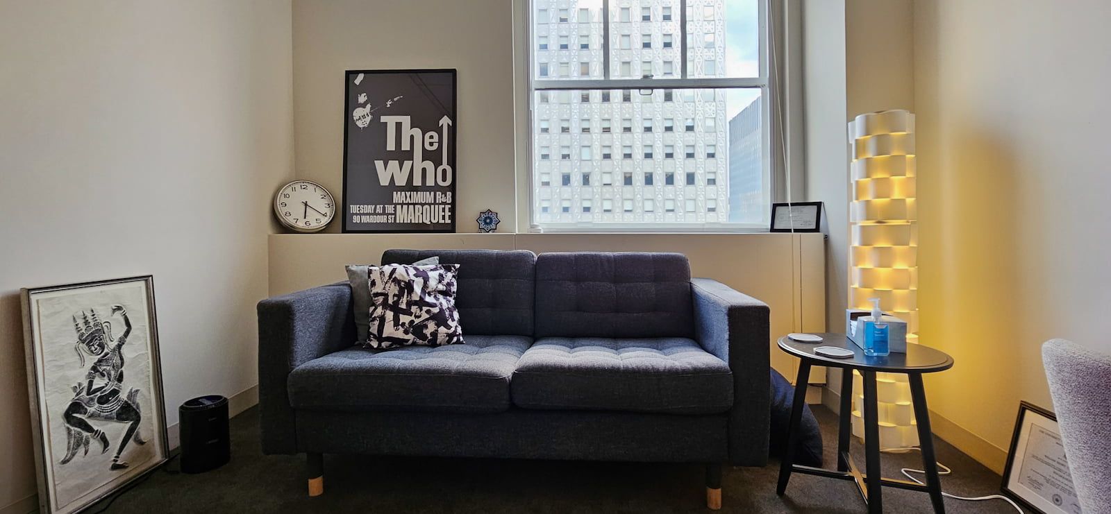 Dr. Gottdiener's office with a cozy couch against a large window, a small end table to the left, and adorned with framed prints and a few ornaments.